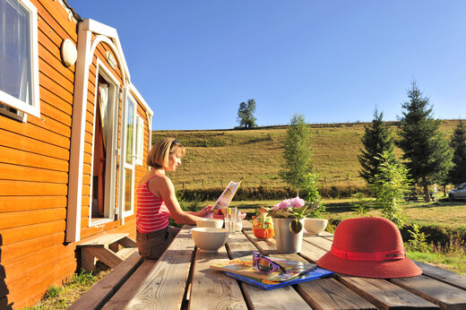 Woman reading at outdoor table in front of wooden Mobile-home at CAPFUN Oursi�re campsite in Villard de Lans (38).