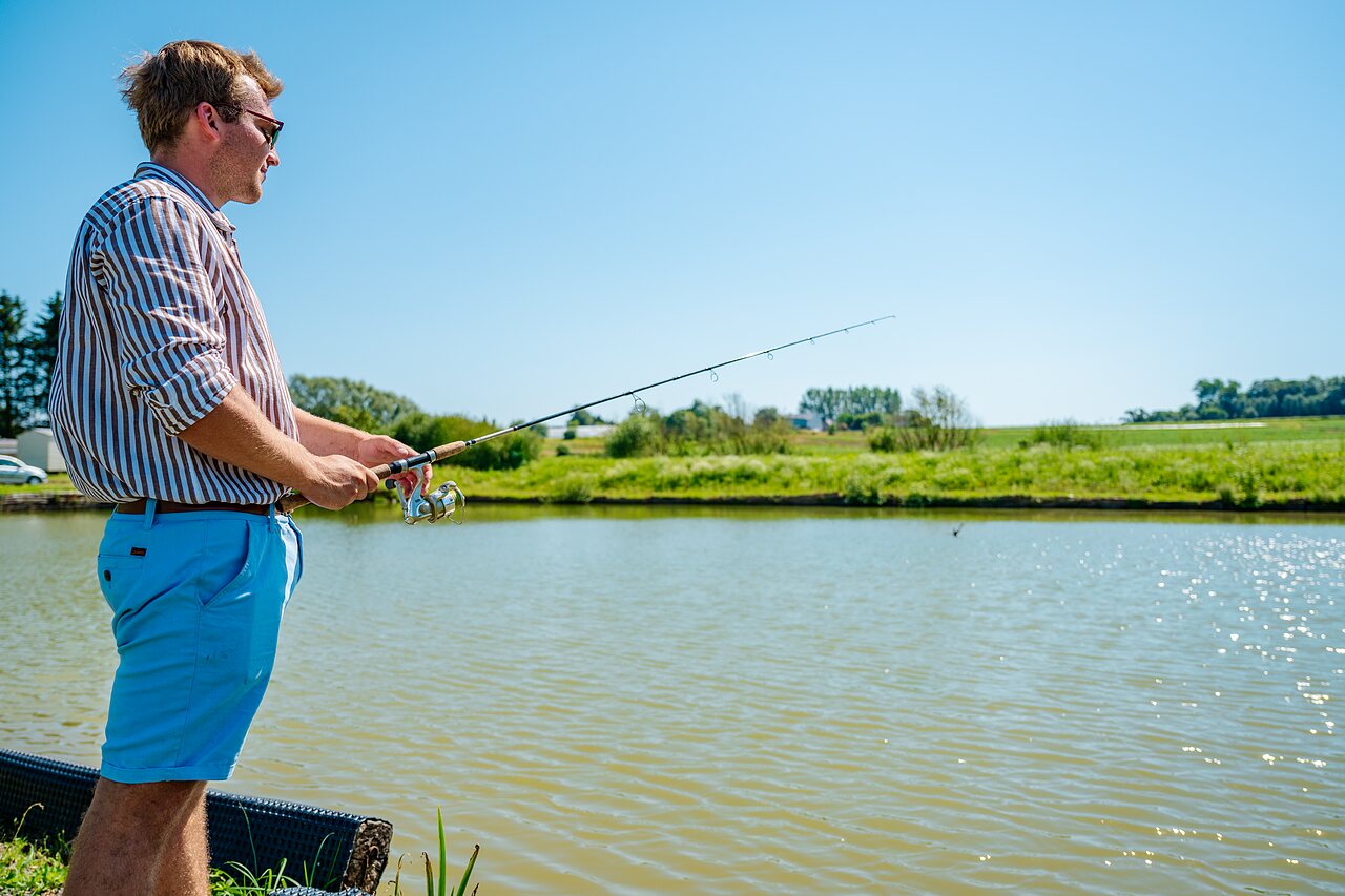 Man fishing by sunny pond at CAPFUN Pachy campsite, FOSSES LA VILLE.