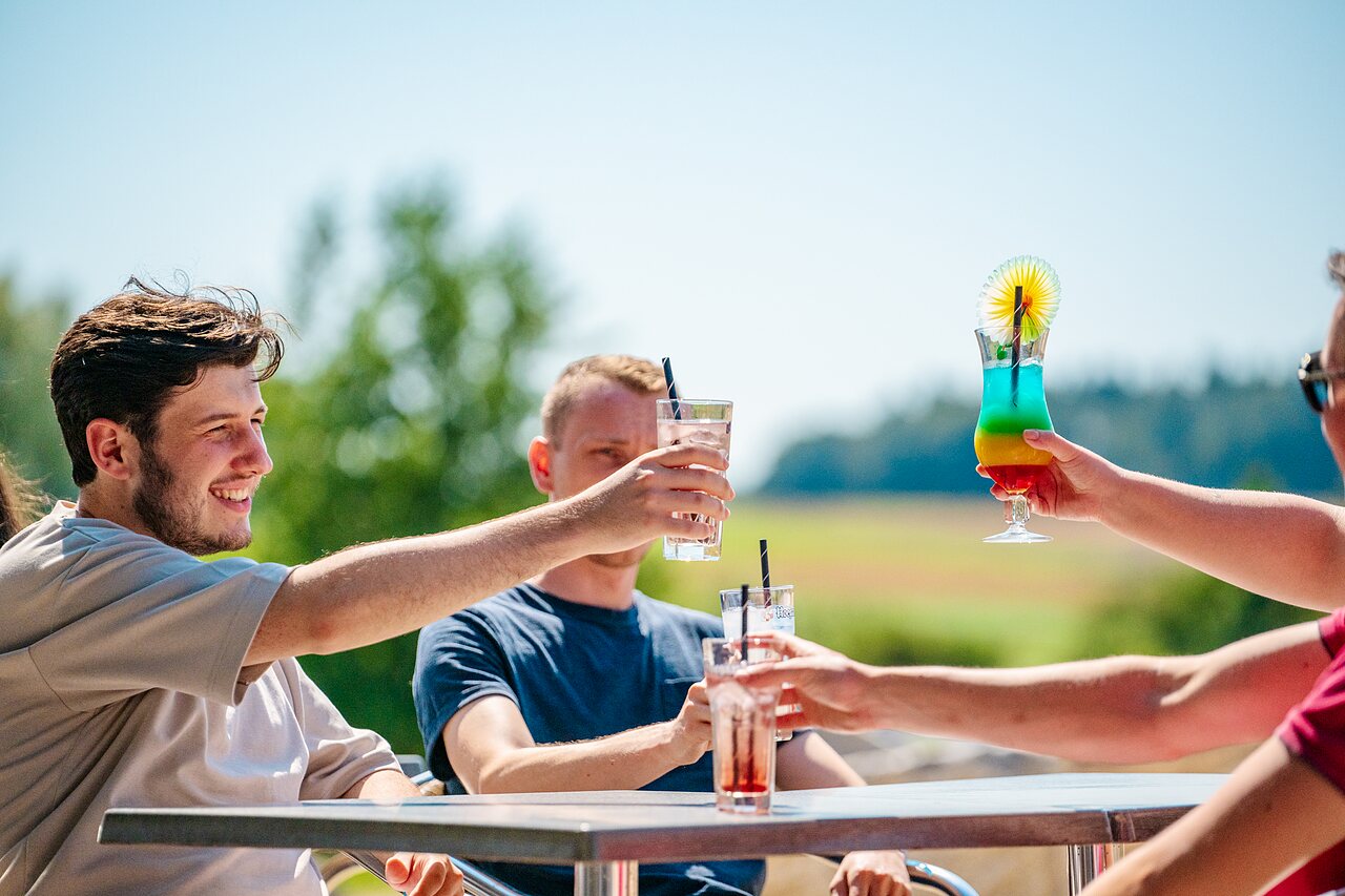 Friends toasting with colorful cocktails at the bar of CAPFUN Pachy campsite in FOSSES LA VILLE.