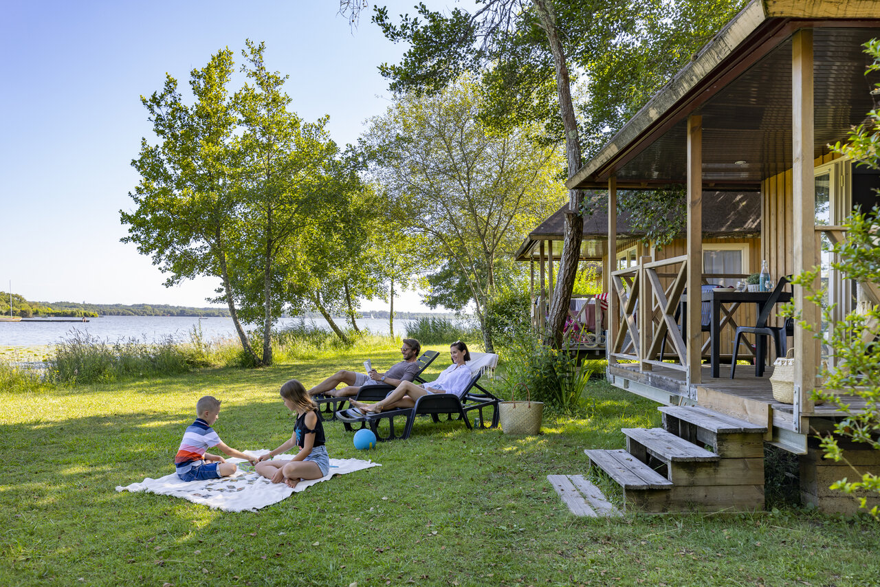 Family relaxing in front of a Mobil-home by the lake, at CAPFUN Paillotte campsite in AZUR (40).