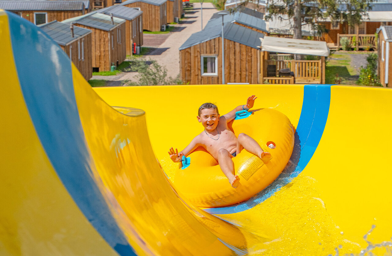 Smiling child on tube, yellow water slide at CAPFUN Palais de Gaufrette campsite.