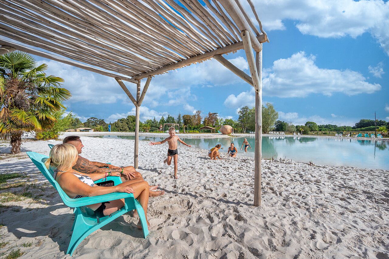 Family enjoying sandy beach and lagoon at CAPFUN Paradis de Bazas campsite in BAZAS (33).