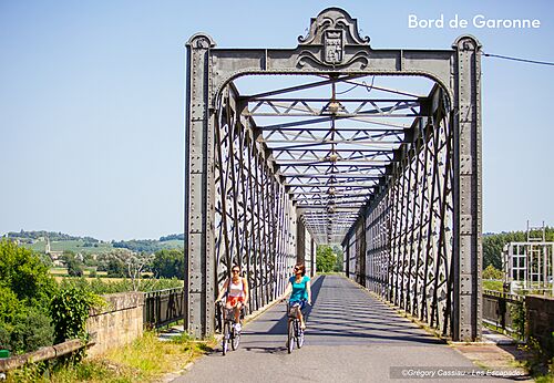 Two people cycling on metal bridge near Garonne river, Bazas.