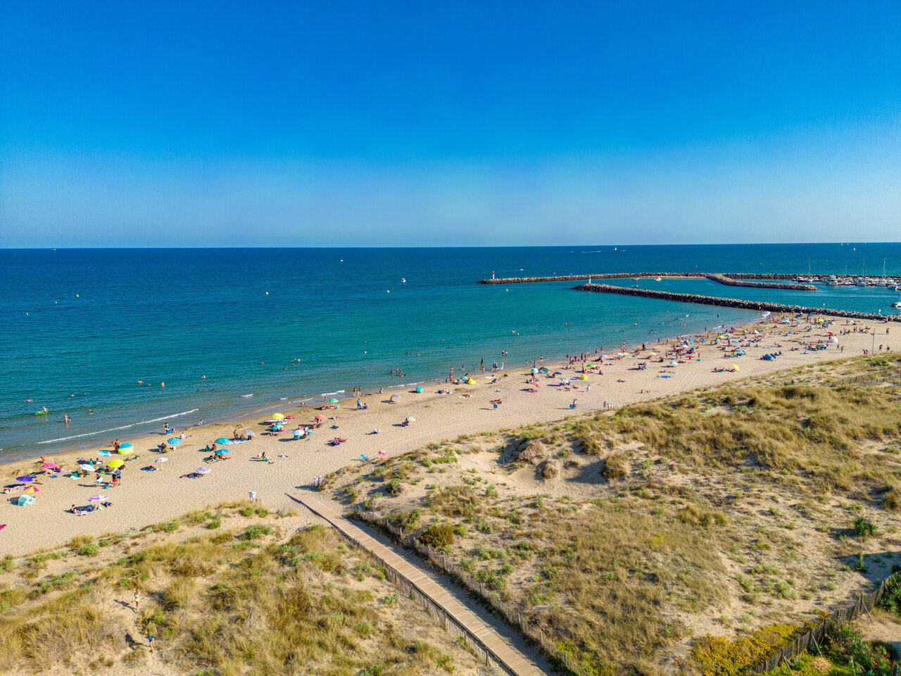 Fine sandy beach, swimmers and marina at CLICOCHIC Paradou campsite.