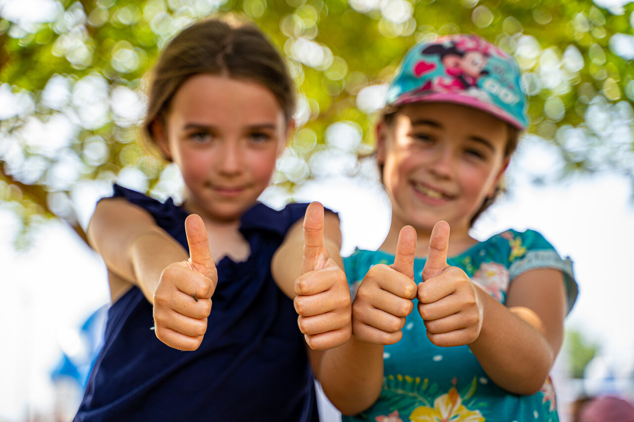Two happy girls giving thumbs up at camping CLICOCHIC Paradou, Marseillan-Plage (34).