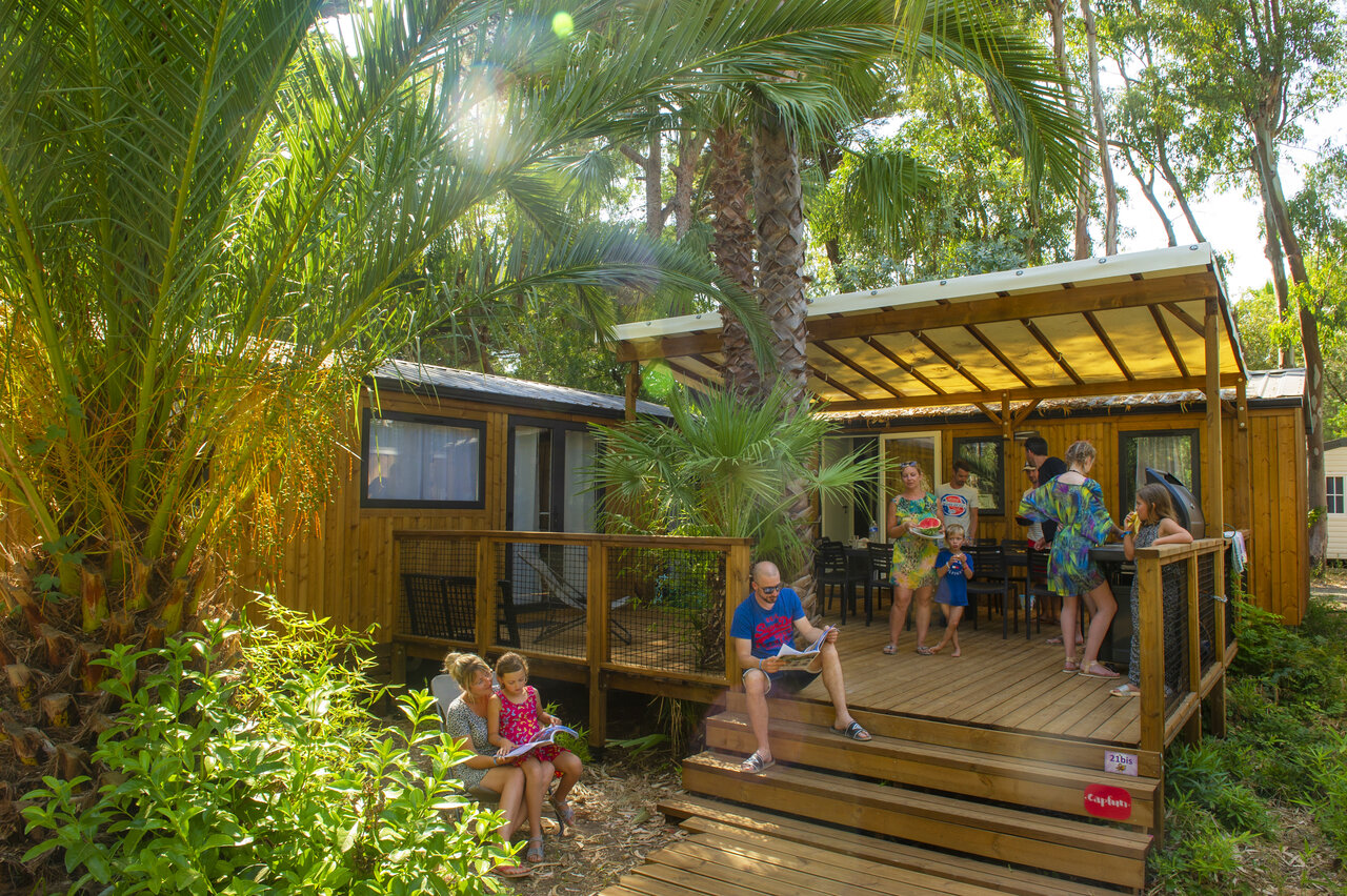 Relaxed family in front of modern Mobile home with terrace at CAPFUN Parc et Plage campsite in Hy�res les Palmiers.