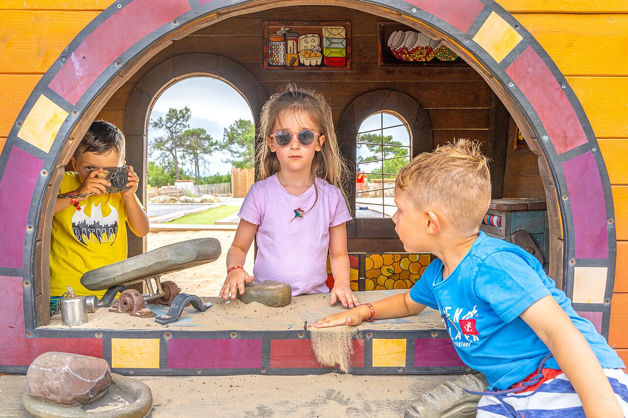 Children playing in a playground with sand and wooden playhouse at camping CLICOCHIC Petit Nice in PYLA SUR MER (33)