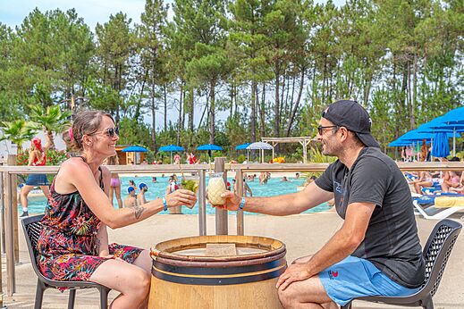Smiling couple enjoying drinks at the pool bar at CAPFUN Pin�da campsite in CAZAUX (33).