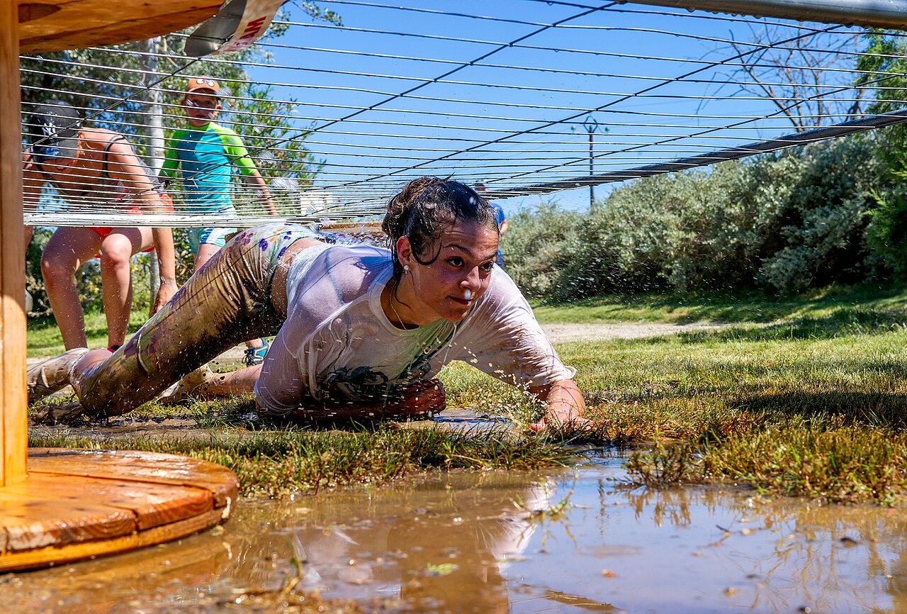 Woman crawling, muddy obstacle course at CAPFUN Plantas campsite in SAINT VINCENT DE DURFORT (07).