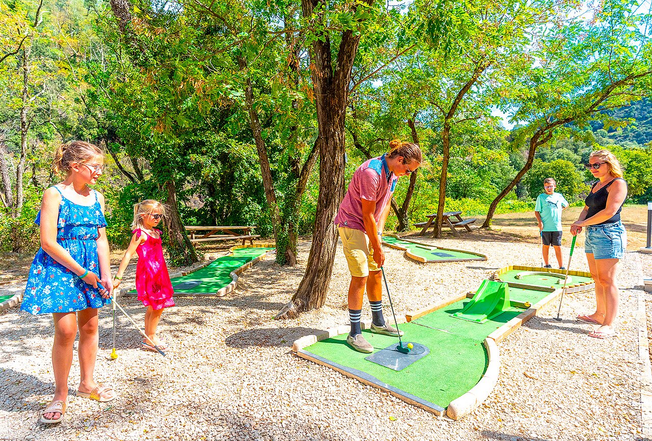 Family playing mini-golf on shaded course at CAPFUN Plantas campsite in SAINT VINCENT DE DURFORT (07).