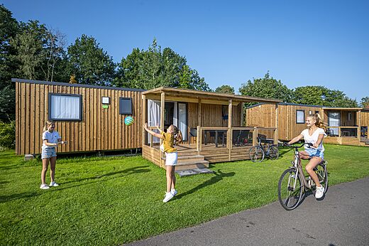 Wooden mobile homes with terrace and children playing at CAPFUN Ponderosa Ulicoten.