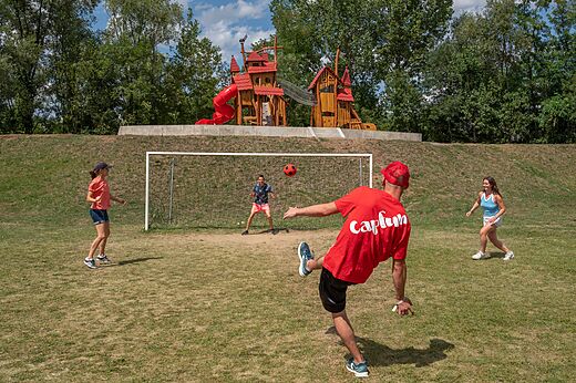 Family playing football on sports field with playground at CAPFUN Les Portes du Beaujolais in Anse (69).