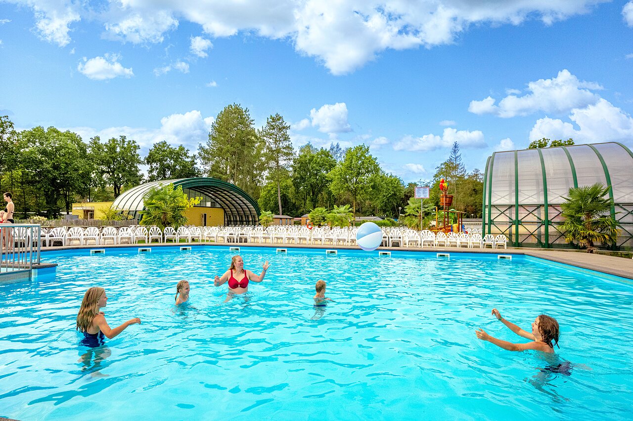 Outdoor pool, family playing with ball, water games at CAPFUN Rakelbos campsite.