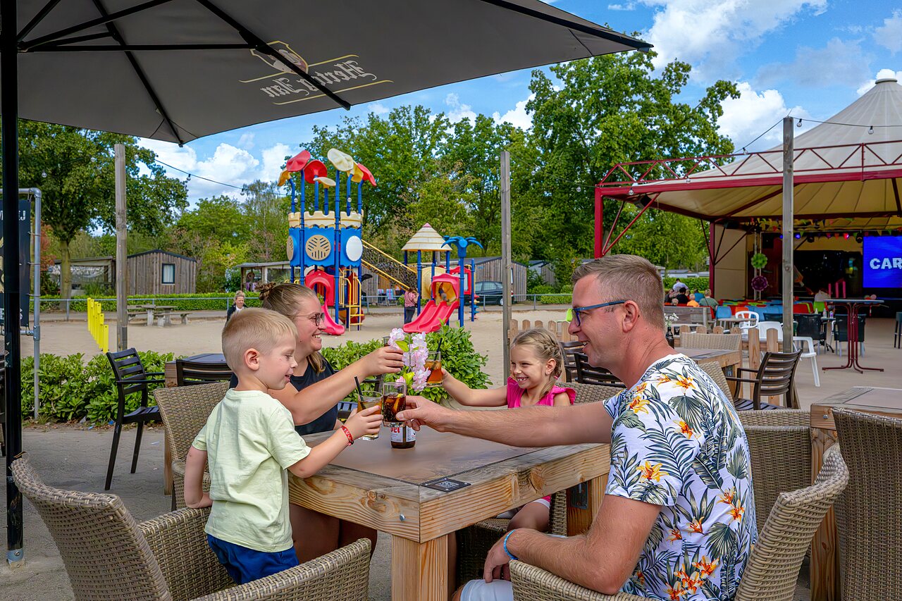 Family toasting near playground and animation stage at CAPFUN Rakelbos campsite in Westelbeers.