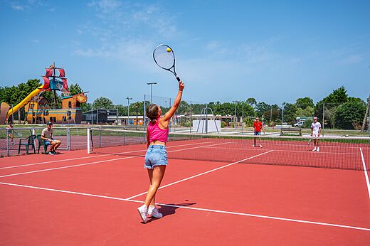 Red tennis court with players at CAPFUN Roumingue campsite, LANTON (33).