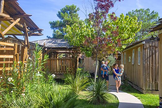 Family walking near wooden accommodations at CAPFUN Sagittaire campsite in VINSOBRES (26).