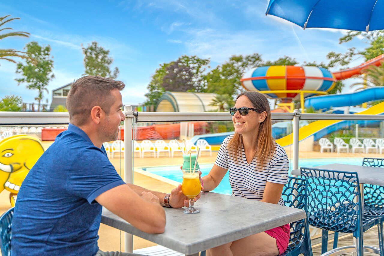 Couple at bar, pool and slides at CAPFUN Saint Laurent campsite in LA FORET FOUESNANT (29).