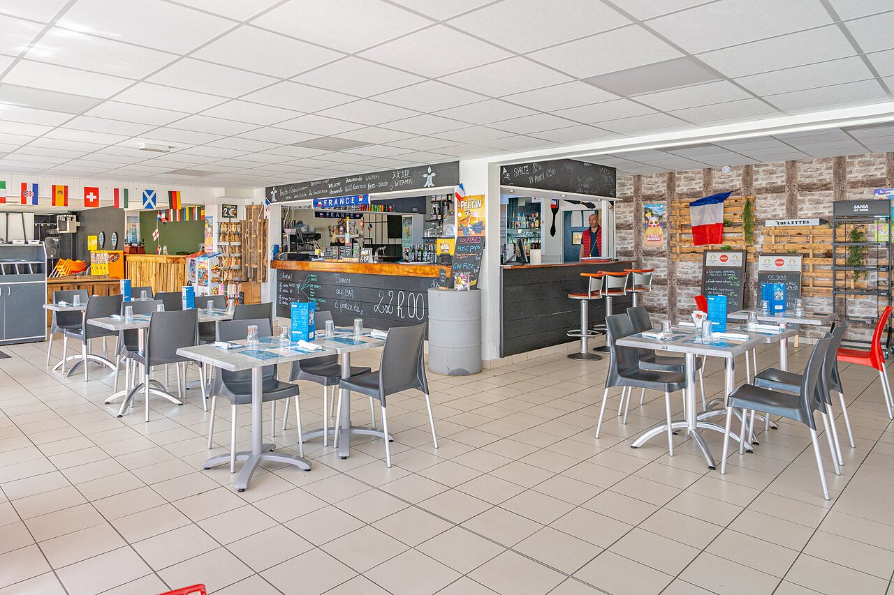 Bar and indoor restaurant area with tables at CAPFUN Saint Laurent campsite in LA FORET FOUESNANT (29).