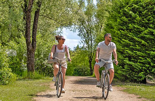 Couple cycling on green path at CLICOCHIC Les Saules de Cheverny campsite.