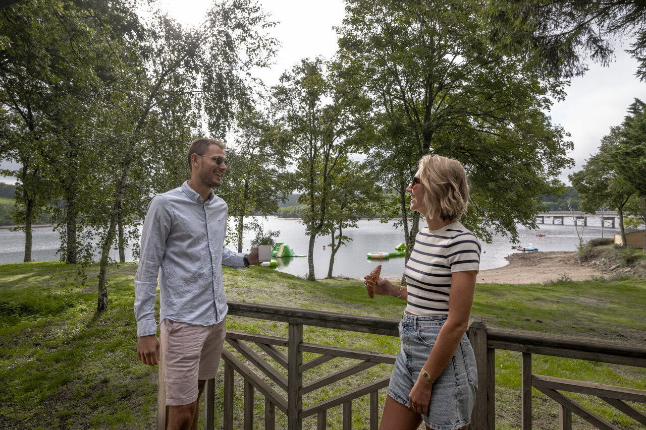 Couple on terrace, lake, water activities at camping CLICOCHIC Soleil Levant in Canet-de-Salars.