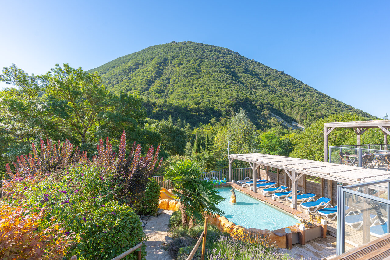 Outdoor pool with slide and sun loungers, green mountain at CLICOCHIC Source du Jabron campsite in Comps (26).