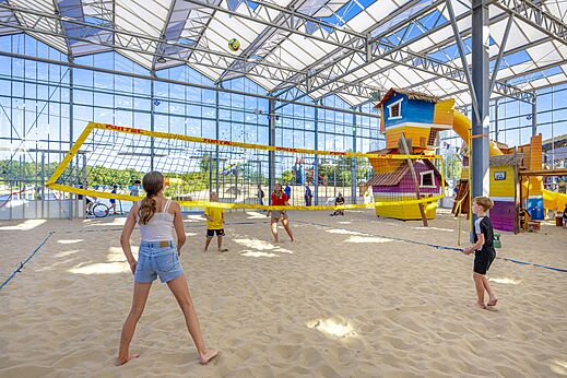 Indoor beach volleyball court with children and adults at campsite CAPFUN Vakantiepark Capfun het Stoetenslagh in Rheezerveen.