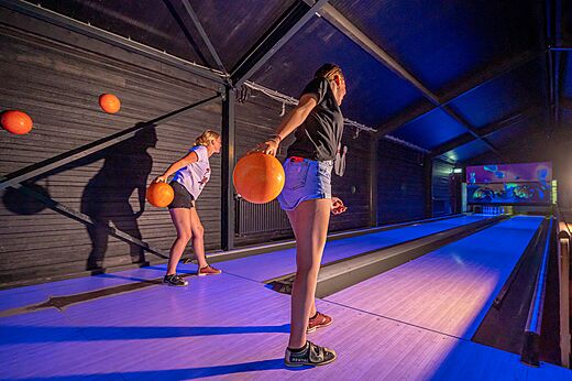 Two young women bowling on a lit lane at CAPFUN Vakantiepark Capfun het Stoetenslagh campsite in Rheezerveen.