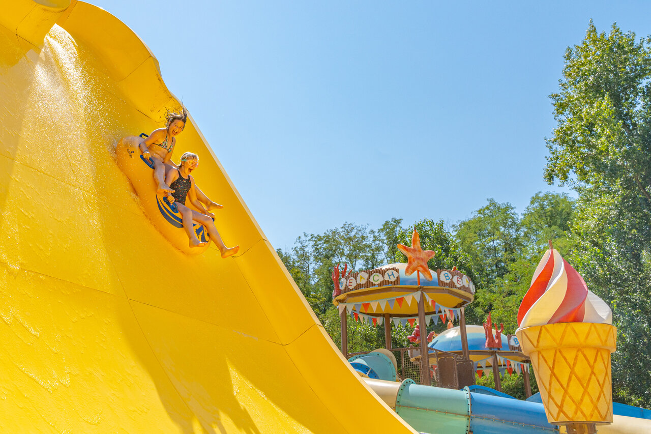 Children sliding down a large yellow water slide at CAPFUN Temps Libre campsite in BOUGE CHAMBALUD (38).