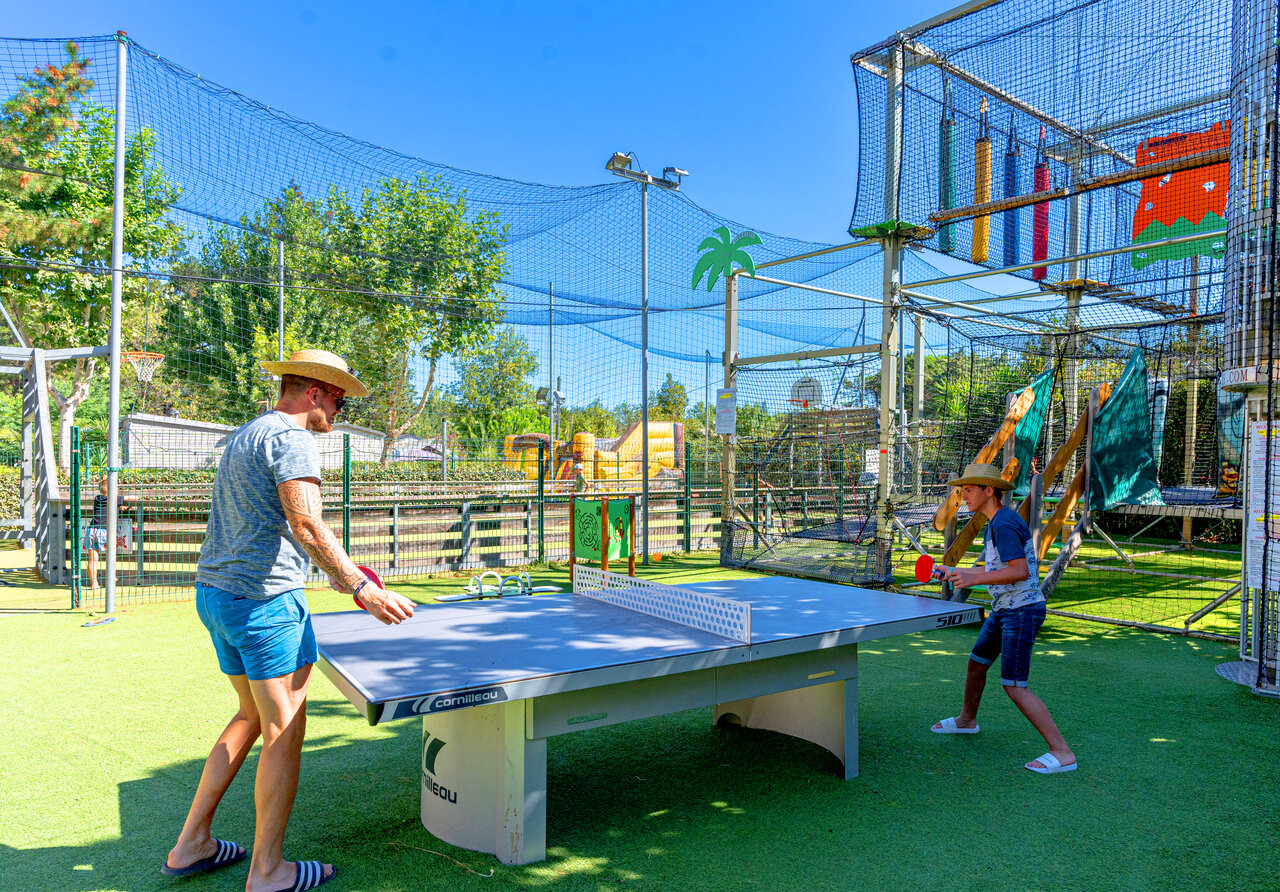 Father and son playing table tennis on artificial grass at CLICOCHIC Texas campsite in Argel�s sur Mer (66).