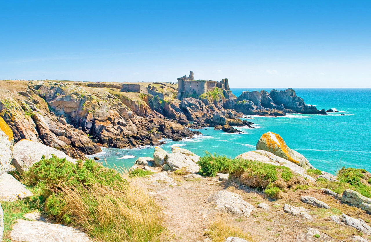 Rocky cliffs, turquoise sea and historic ruins at CLICOCHIC Plage des Tonnelles campsite.