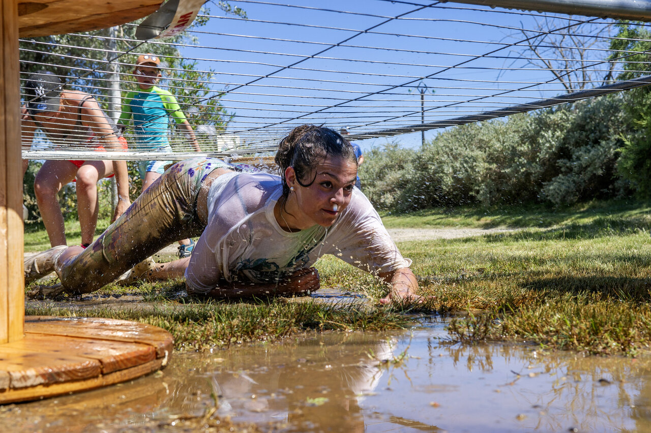 Woman crawling through muddy obstacle course, animation at CAPFUN Tordera-Nacions campsite in Malgrat de Mar.