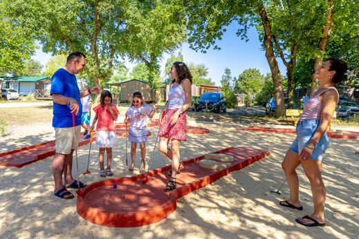 Family playing mini-golf on a sandy course at CAPFUN Celeste campsite in Breuillet (17).