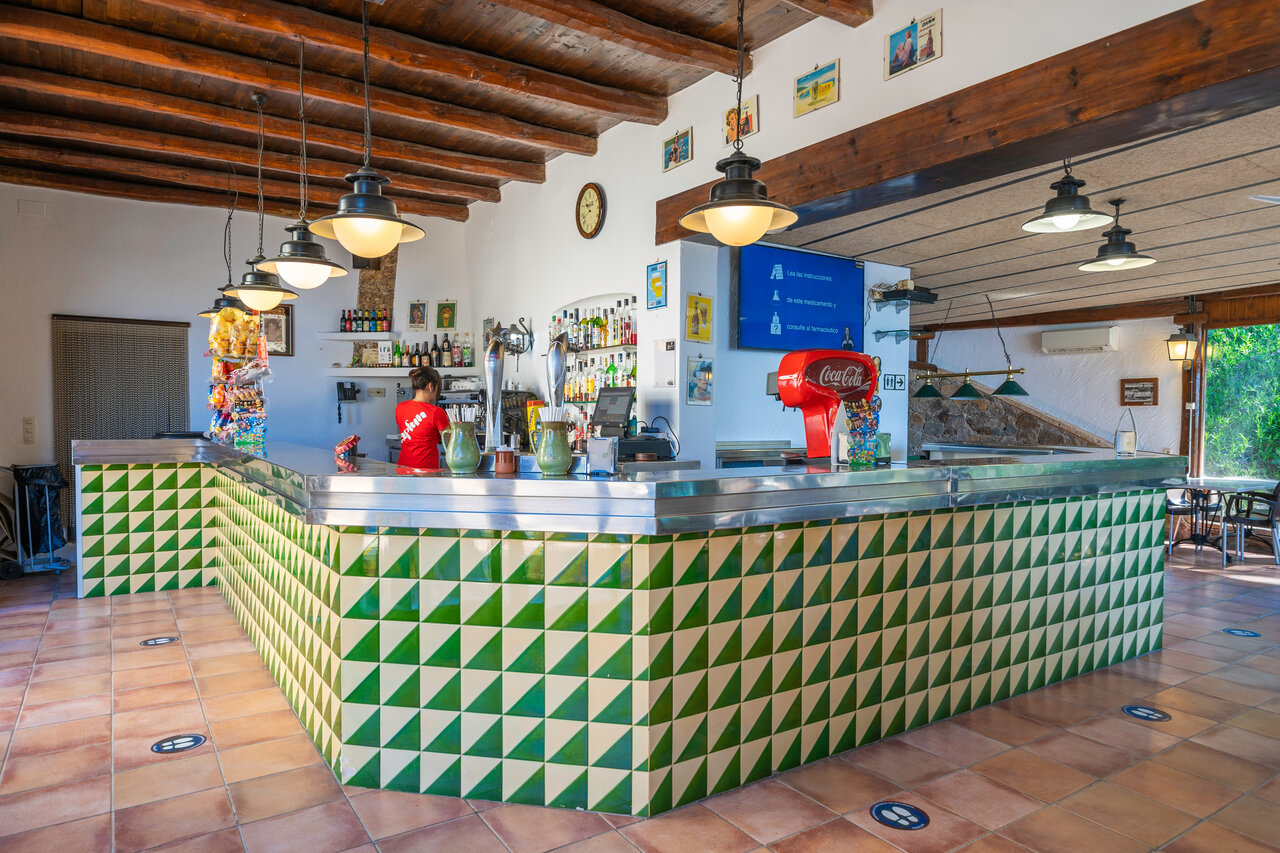 Indoor bar with counter and waitress at CAPFUN Treumal campsite in Platja d'Aro.