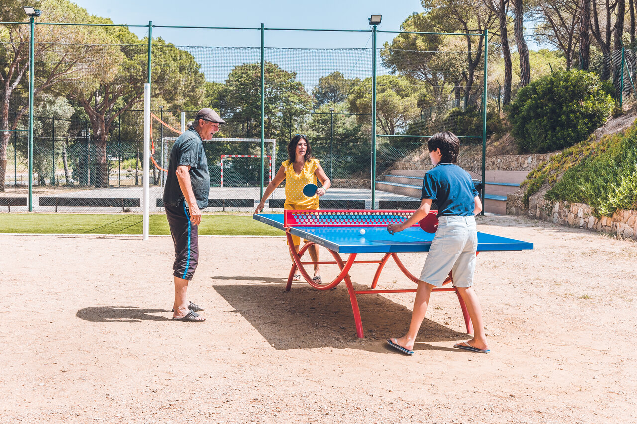 Family playing table tennis outdoors at CAPFUN Treumal campsite in Platja d'Aro.