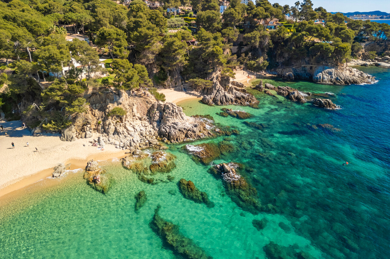 Fine sandy beach, rocky coves, and turquoise sea at CAPFUN Treumal campsite.
