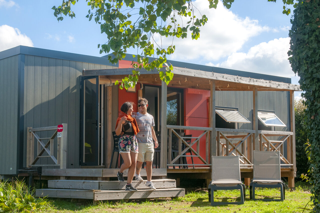 Modern mobile home and smiling couple on the terrace at CAPFUN Vikings campsite in Saint Jean de la Rivi�re (50).