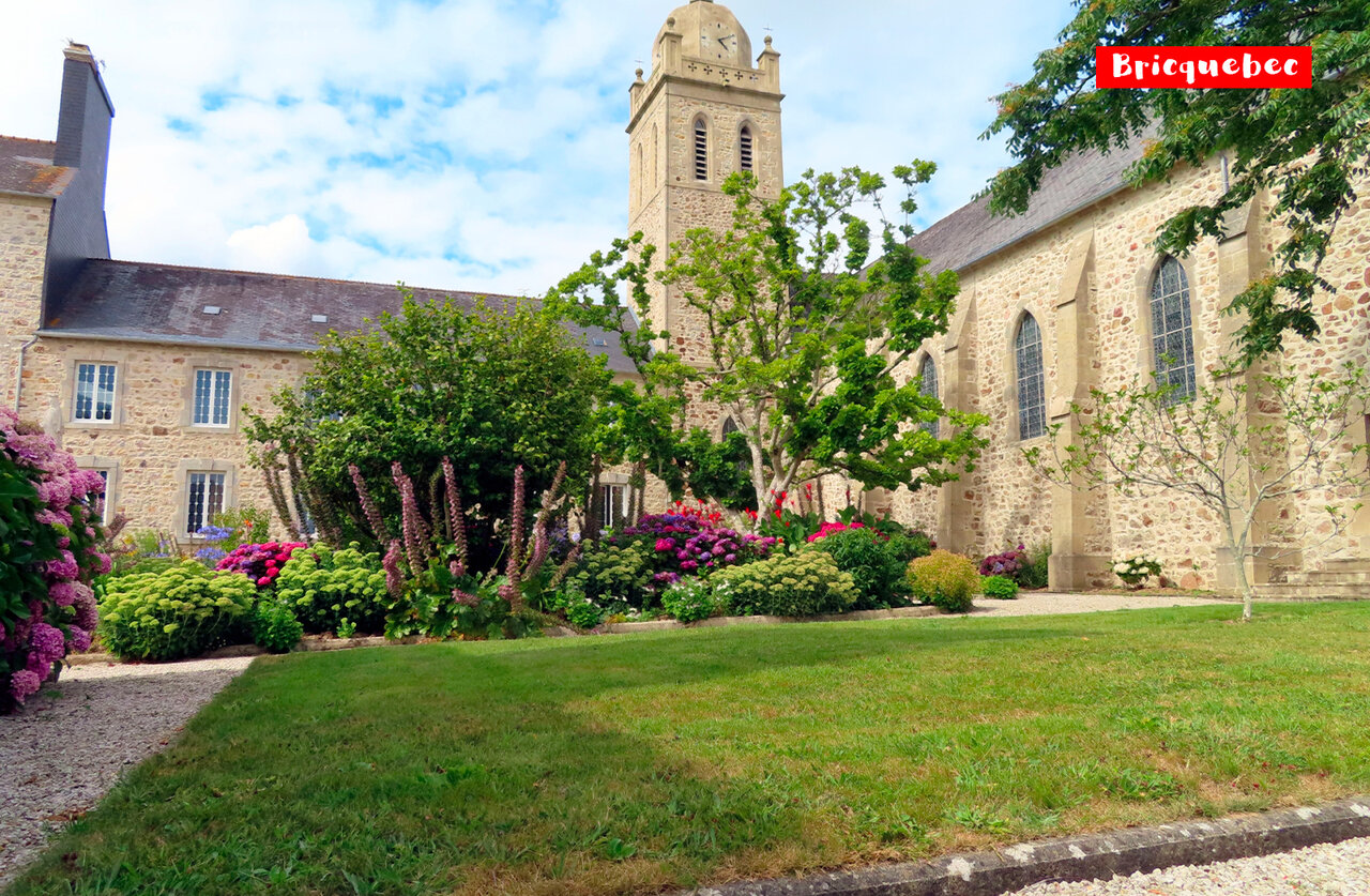 Historic church with bell tower and flowered gardens in Bricquebec, Normandy.