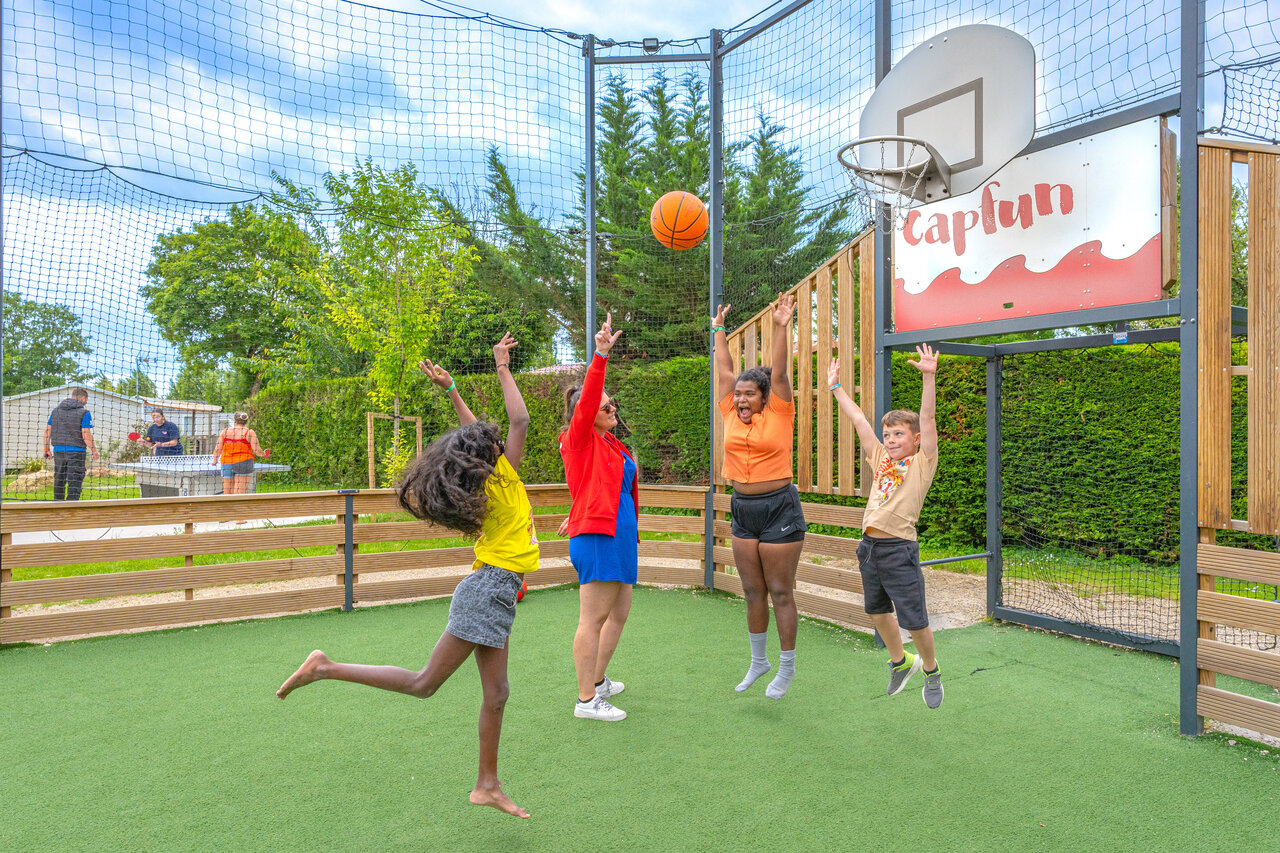 Children and adults playing basketball on multisport court at CAPFUN Le Village Parisien campsite in VARREDDES (77).