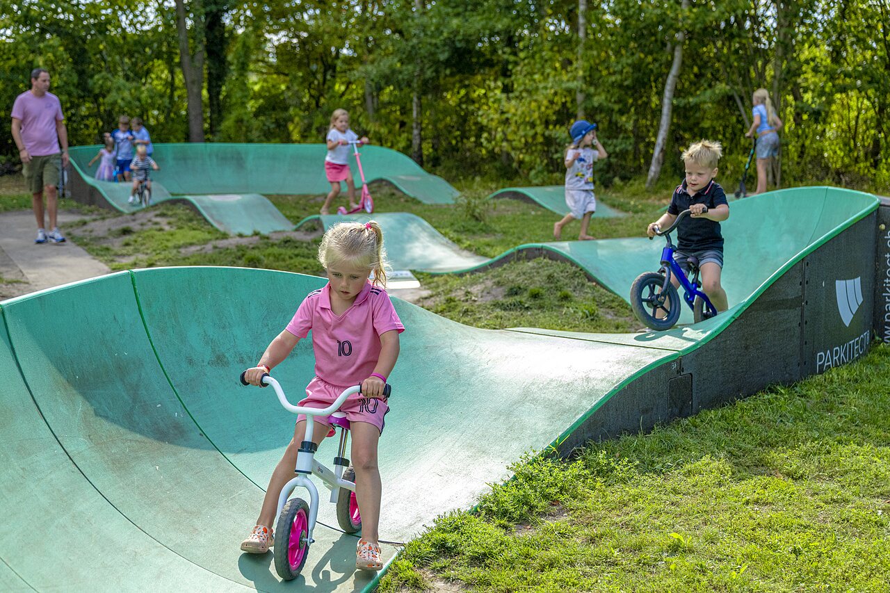 Children playing on the pump track with bikes and scooters at CAPFUN Vlinderloo campsite in Enschede.