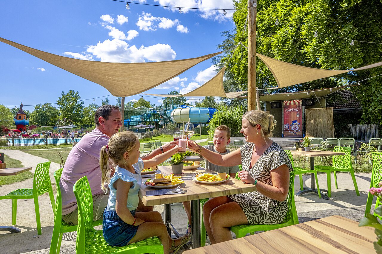 Family dining on terrace, pool and slides at CAPFUN Vlinderloo campsite in Enschede.