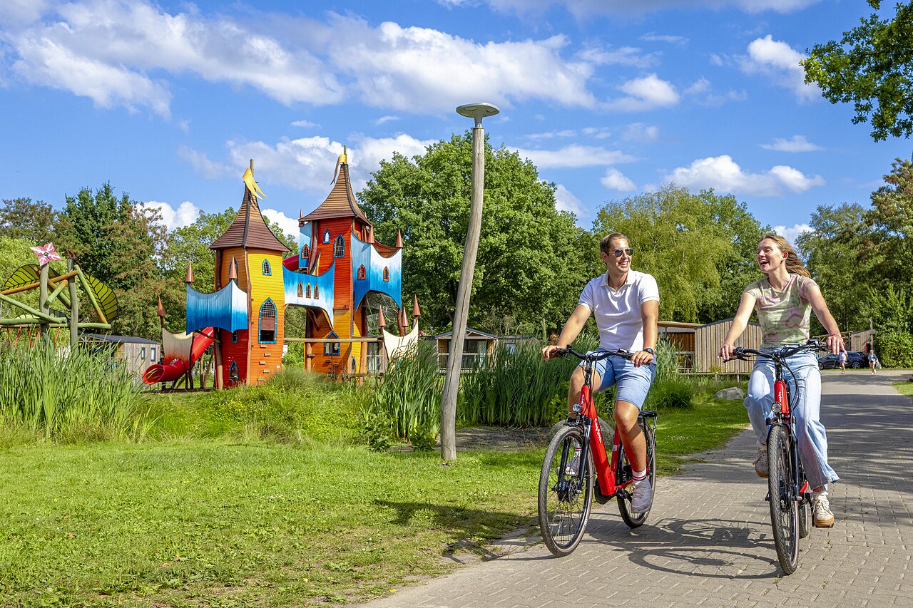 Colorful castle playground and couple cycling at CAPFUN Vlinderloo campsite in Enschede.