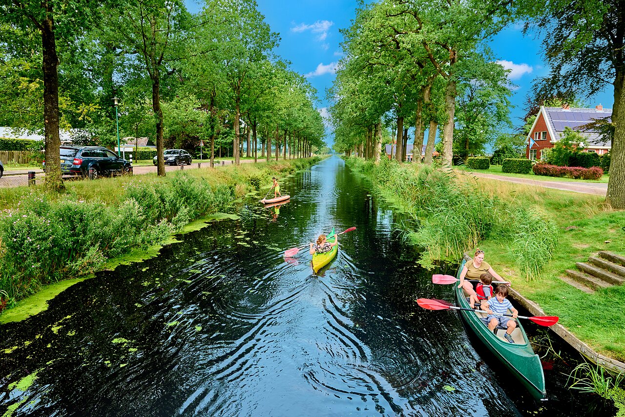 Family in canoe and paddleboard on tree-lined canal at CAPFUN De Waldsang campsite in Bakkeveen.