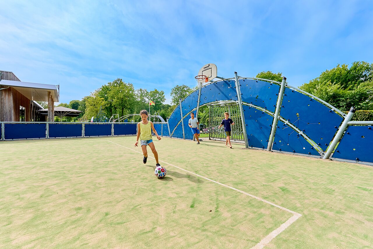 Multi-sport field with children playing soccer, basketball hoop at CAPFUN De Waldsang campsite in Bakkeveen.