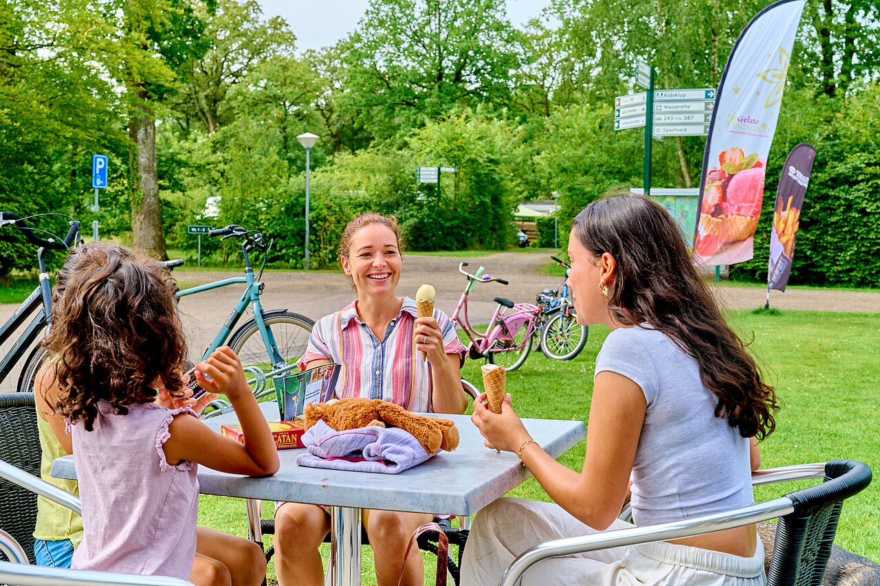 Smiling family eating ice cream on terrace, bicycles, at CAPFUN De Waldsang campsite in Bakkeveen