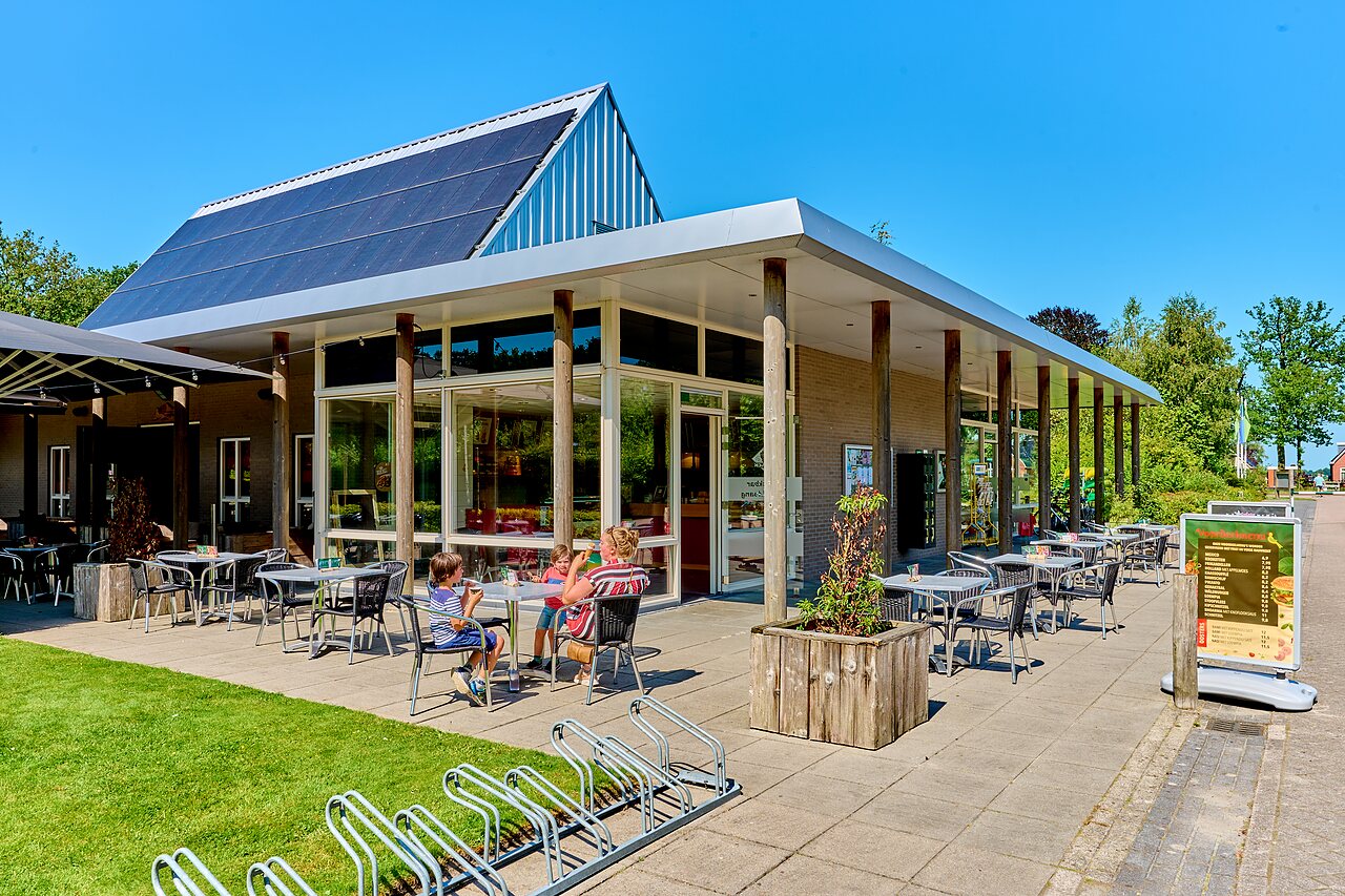 Sunny restaurant terrace, family, solar panels at CAPFUN De Waldsang campsite in Bakkeveen.