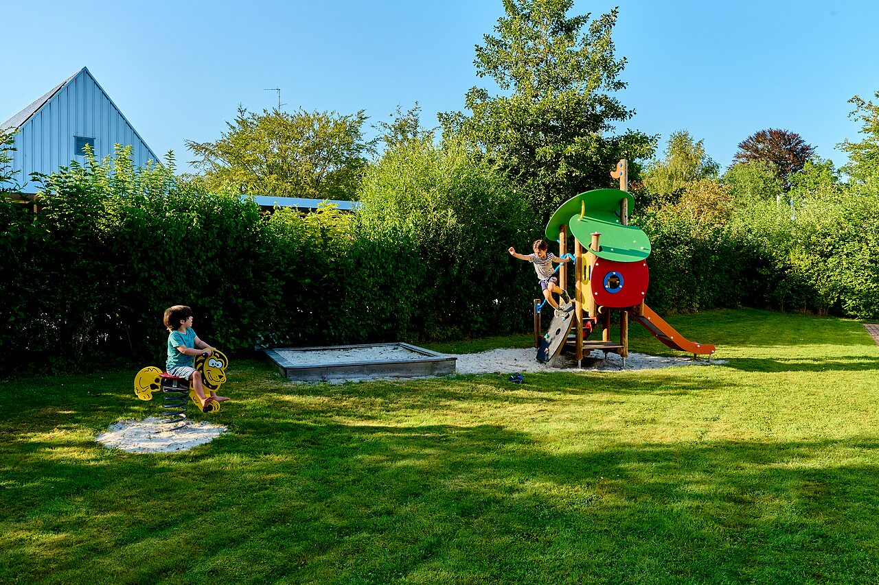 Playground with slide, climbing frame and child on spring rider at CAPFUN De Waldsang campsite in Bakkeveen.
