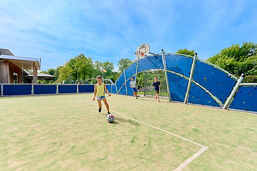 Children playing football on the multi-sport court at CAPFUN De Waldsang campsite in Bakkeveen.