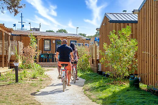 Couple cycling on a path between Mobile homes at CAPFUN Zagarella campsite in LONGEVILLE SUR MER (85).