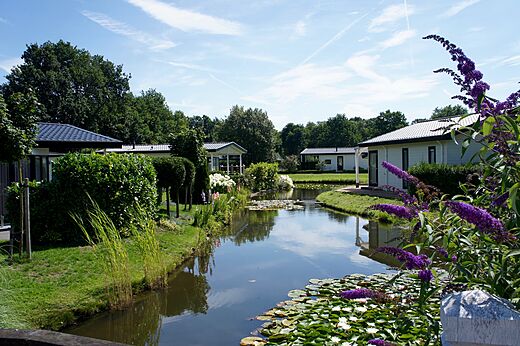 Modern mobile homes by a flowery canal at CAPFUN Zeumersehof campsite in Voorthuizen.